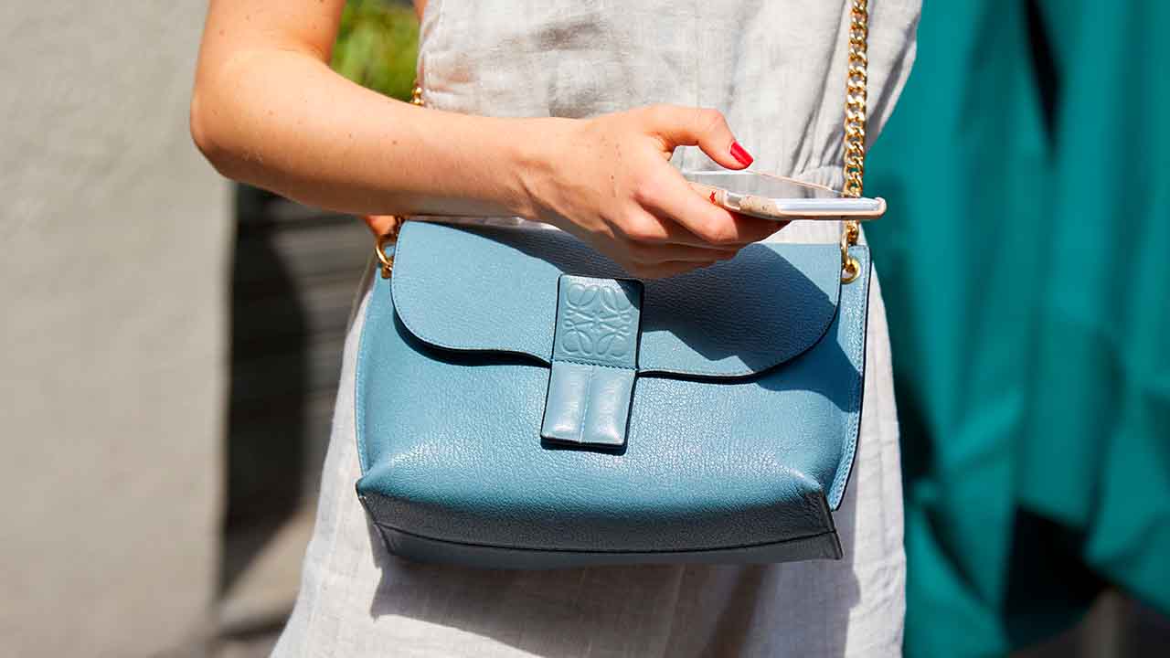 Mulher sesgurando celular na mão, usando vestido e bolsa da marca Loewe.