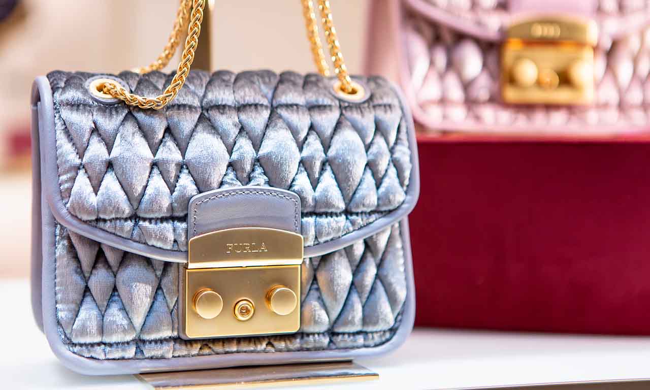 Imagem de uma bolsa da marca Furla feita de tecido metalizado e correntes douradas.