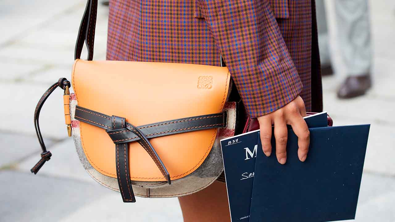 Mulher segurando livros na mão, usando casaco e bolsa da marca Loewe.