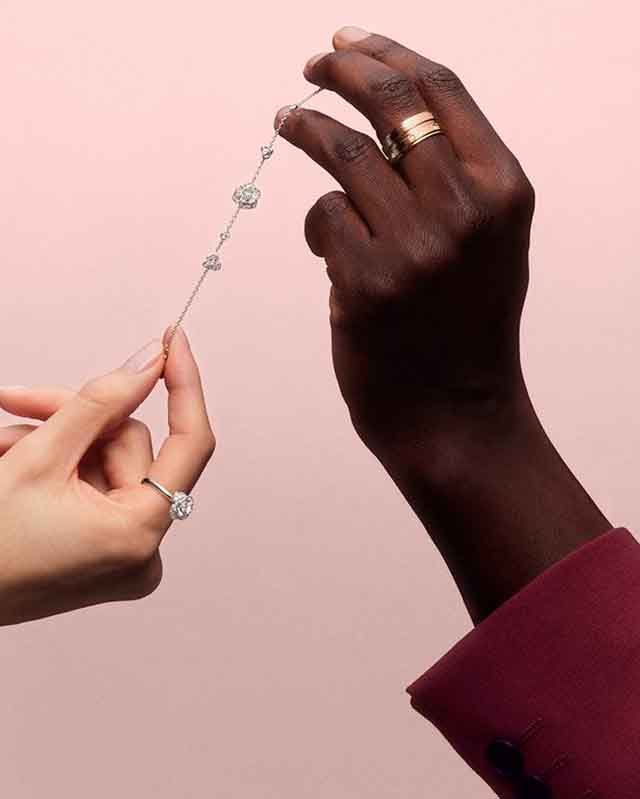 Foto de duas mãos usando anéis e segurando uma pulseira da Piaget.