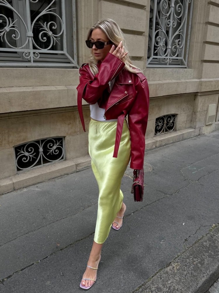 mulher usando saia longa verde de cetim, com blusa branca e jaqueta de couro cropped vermelha