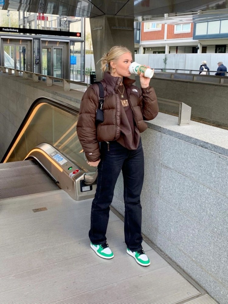 mulher usando calça jeans preta com blusa marrom e jaqueta puffer marrom