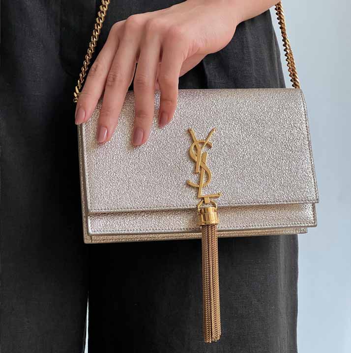 Foto de uma mulher carregando uma bolsa Kate da Saint Laurent: um modelo de bolsa pequena com brilho para usar em festas.
