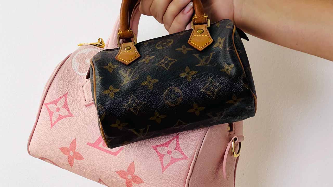 Foto de uma mão segurando duas bolsas com monogramas da Louis Vuitton.