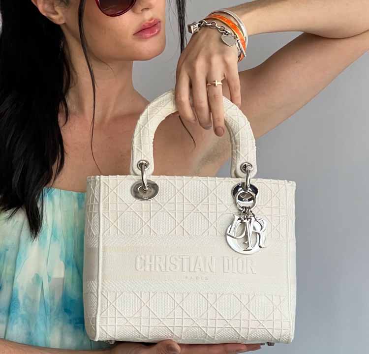 Foto de muher segurando uma das tote bags da Dior, a Lady Dior, uma das bolsas de mão mais famosas do mundo.