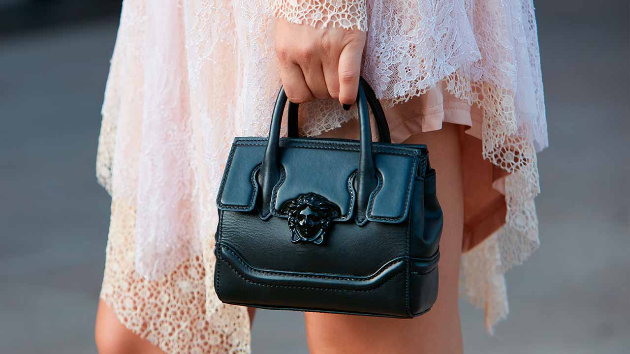 Foto de mulher segurando bolsa pela mão, o acessório possui detalhe de Medusa que é o famoso símbolo da Versace.