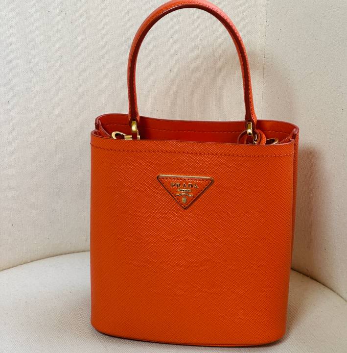 Bolsa Prada Panier em couro Saffiano com acabamento texturizado e triângulo esmaltado Prada na parte frontal.