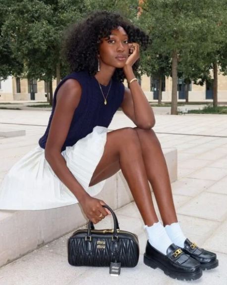 Foto de uma mulher usando mocassim  tratorado com saia curta e meias brancas.