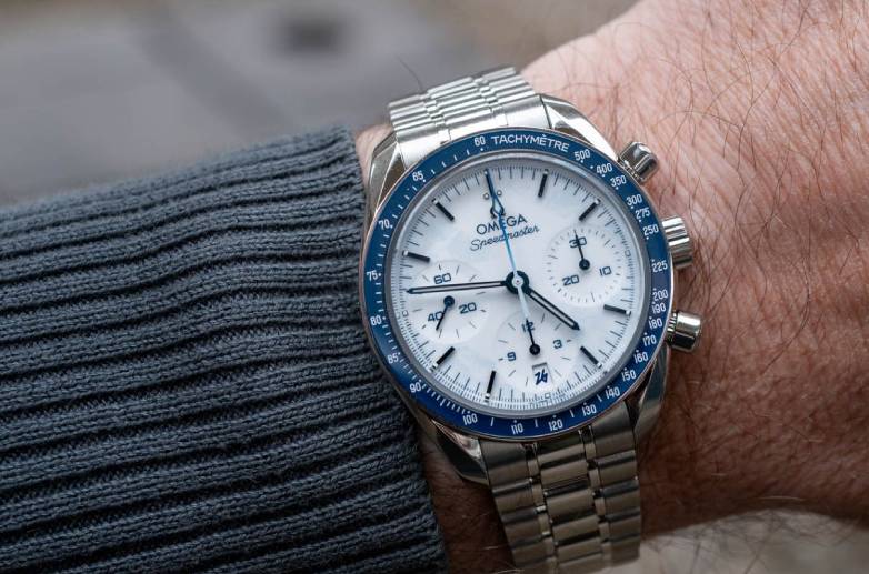 Speedmaster 38mm Milano Cortina no pulso com luneta em cerâmica azul e mostrador branco texturizado.