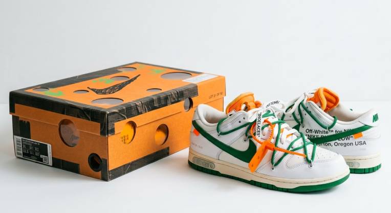 Tênis Nike x Off-White original ao lado da caixa Nike laranja, destacando detalhes de autenticação como qualidade do papelão, impressão fosca e etiqueta SKU correspondente ao modelo.